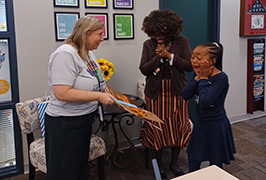  A girl is excited and her mom smiles as as a woman presents her with a book